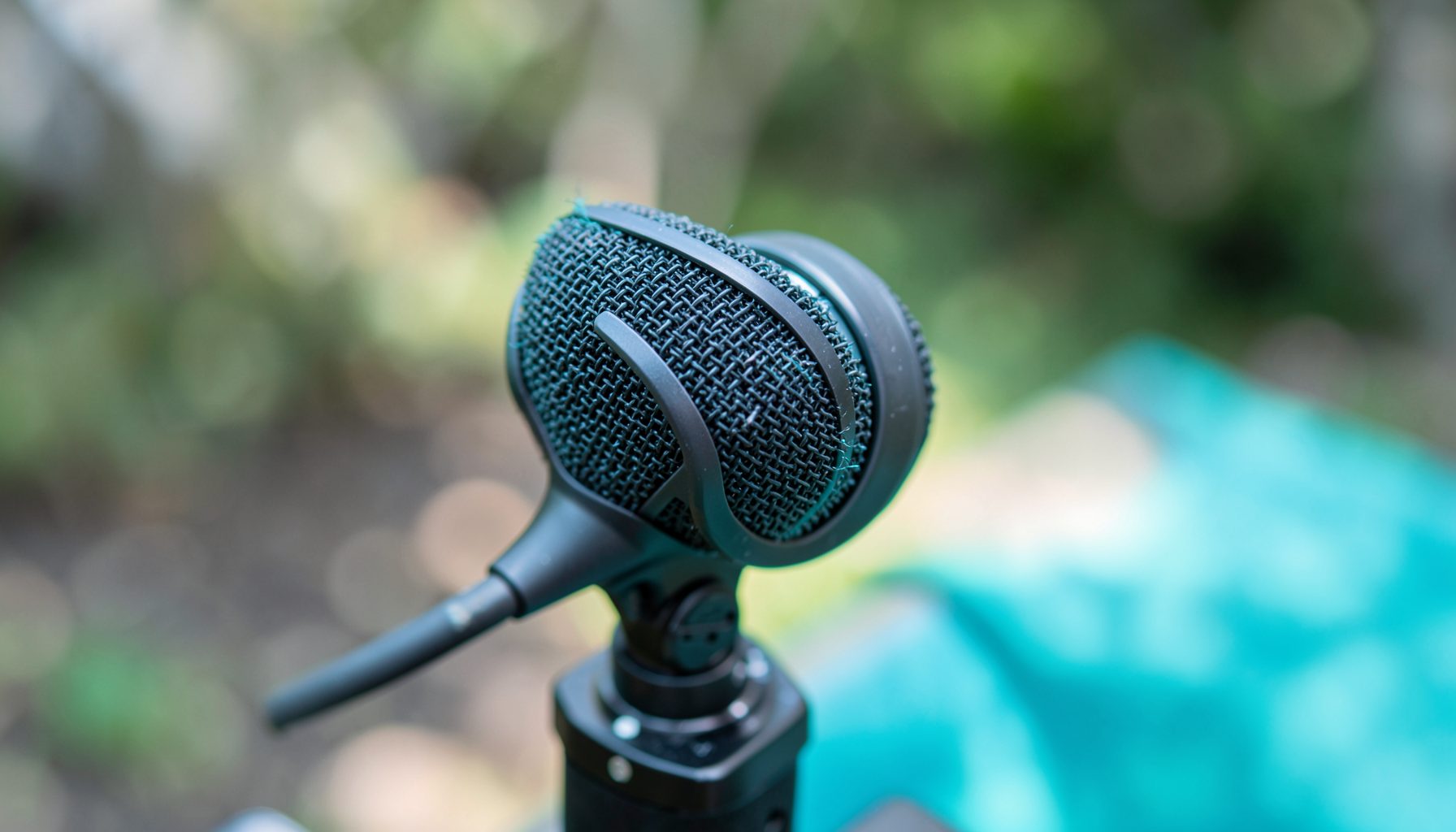 On-camera shotgun microphone mounted on a DSLR, outdoor blurred background