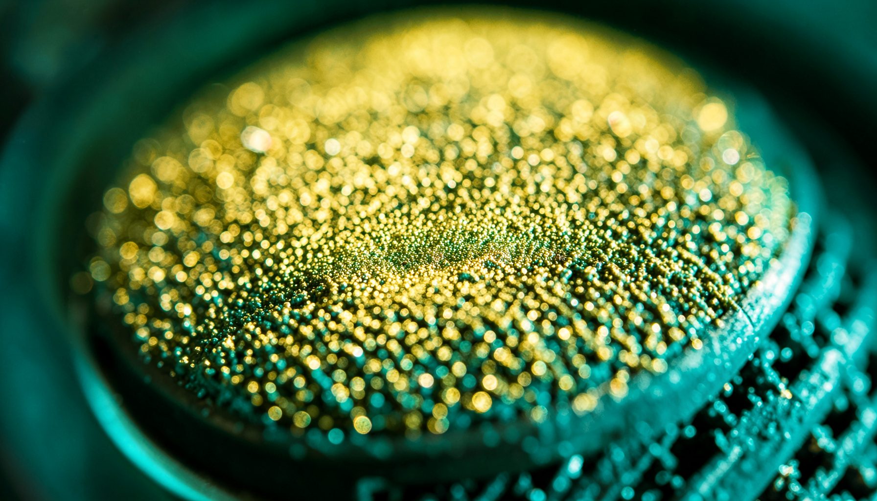 Extreme close-up of a gold-sputtered condenser microphone diaphragm, shimmering metallic surface