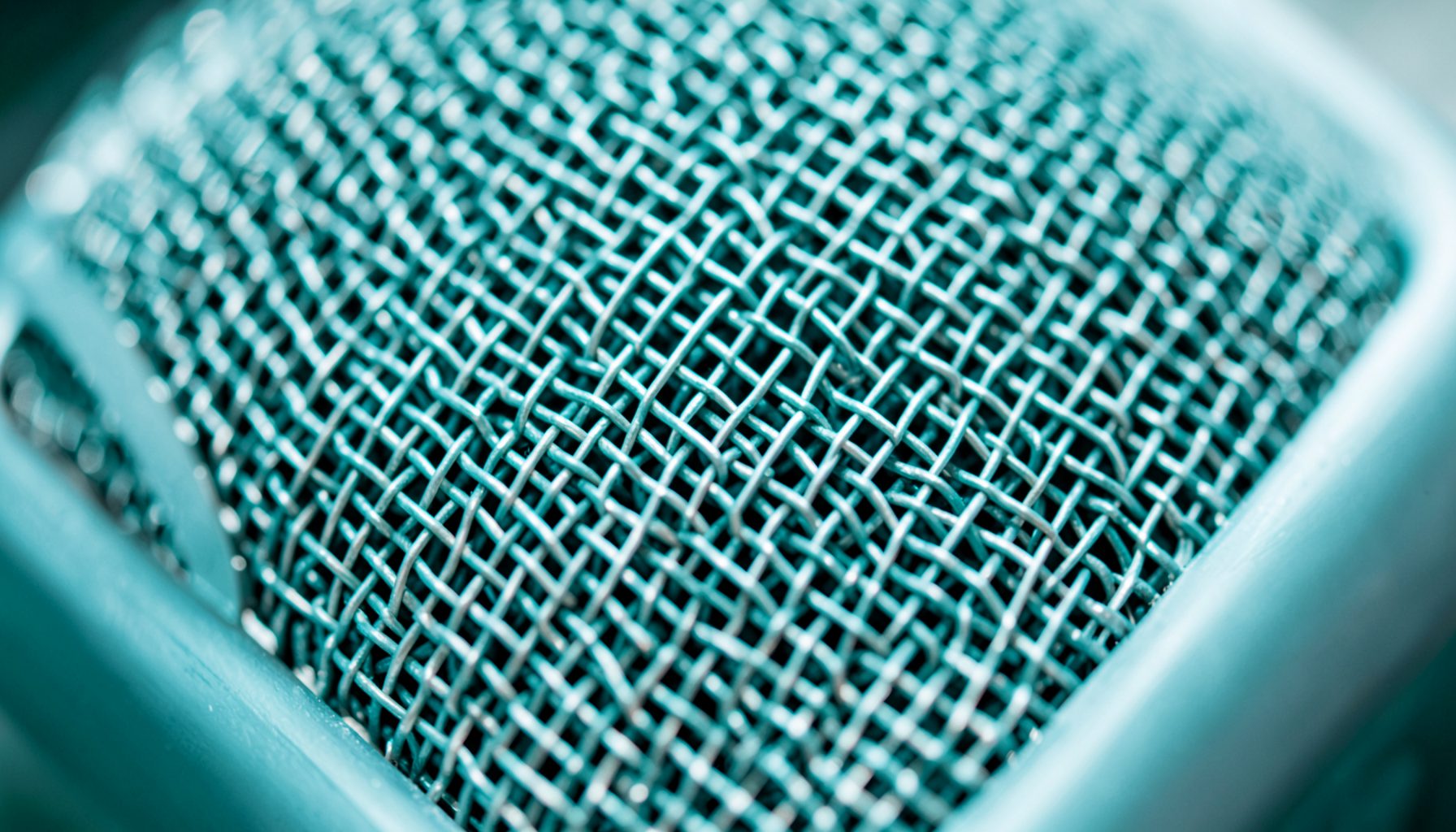 Extreme close-up of a brushed metal microphone grille with fine mesh texture, cool silver tones